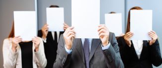 Group of unrecognizable business people covering their faces with sheets of blank paper.