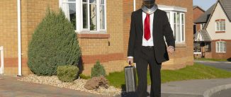 A man in a business suit walking down a street wearing a knight's helmet