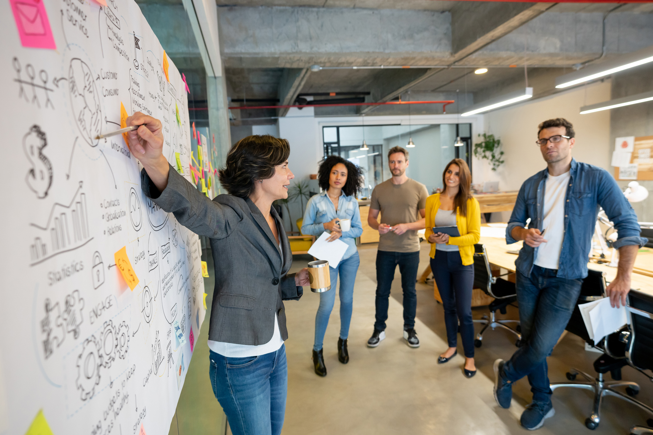 Latin American woman making a business presentation in a meeting at a creative office and pointing to her team her business plan